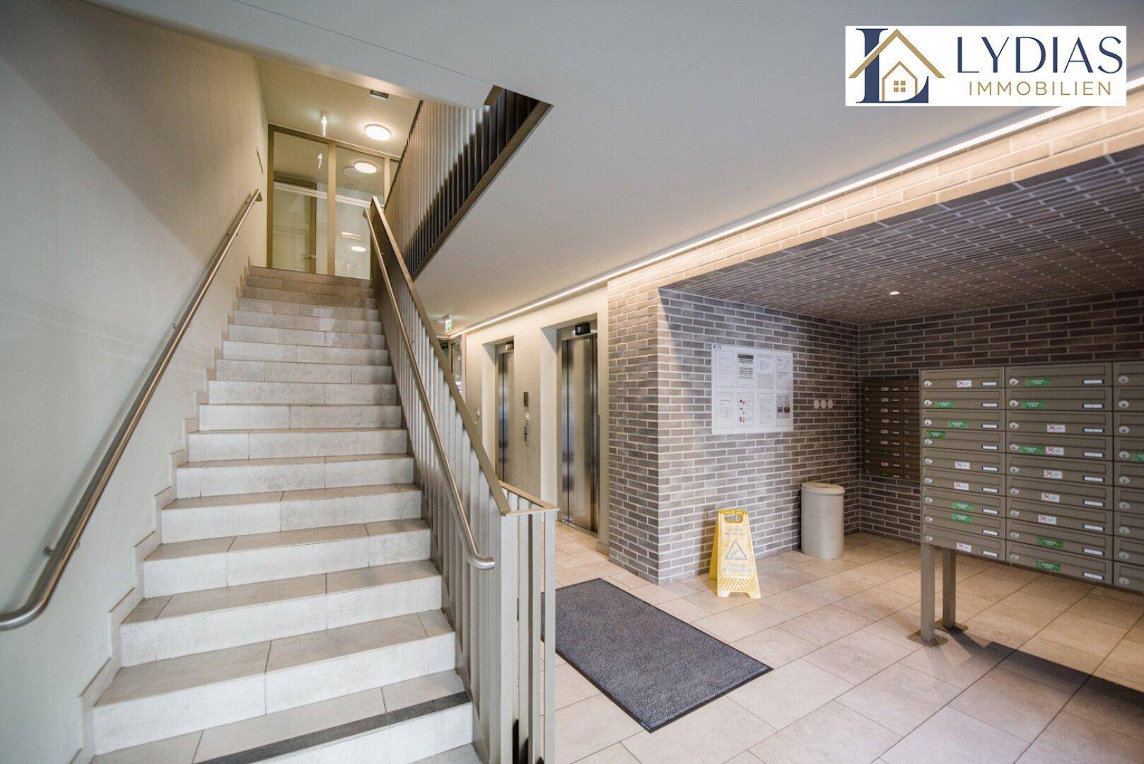 Eingangsbereich eines Mehrfamilienhauses mit Treppe, Aufzügen und Briefkästen.