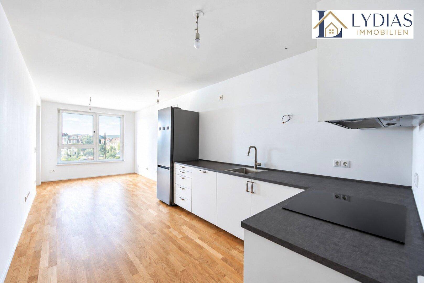 Leere Küche mit Einbauküche, Kühlschrank und Blick ins Grüne durch das Fenster.