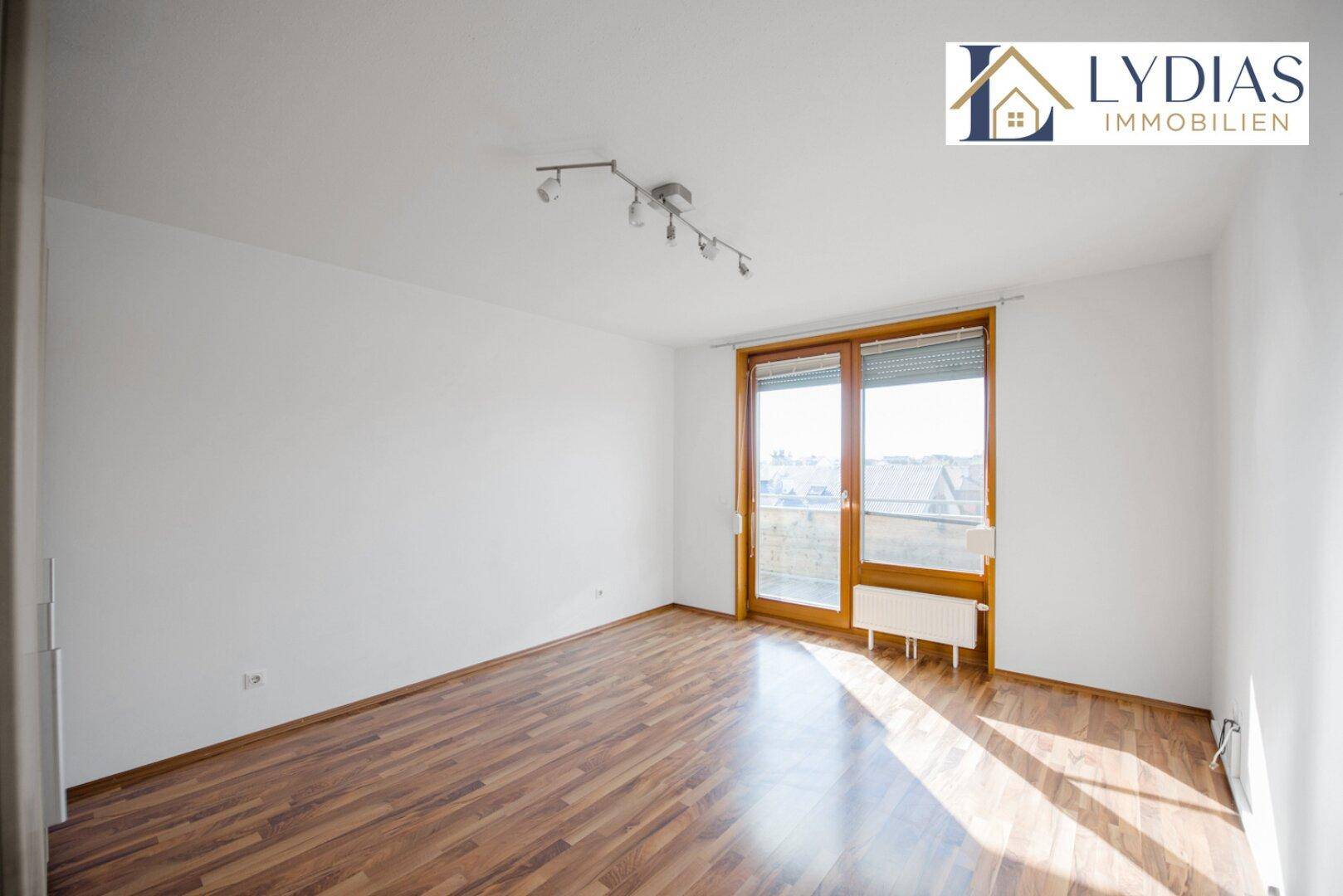 Helles Zimmer mit Holzboden und großem Fenster, bietet Zugang zu einem Balkon.