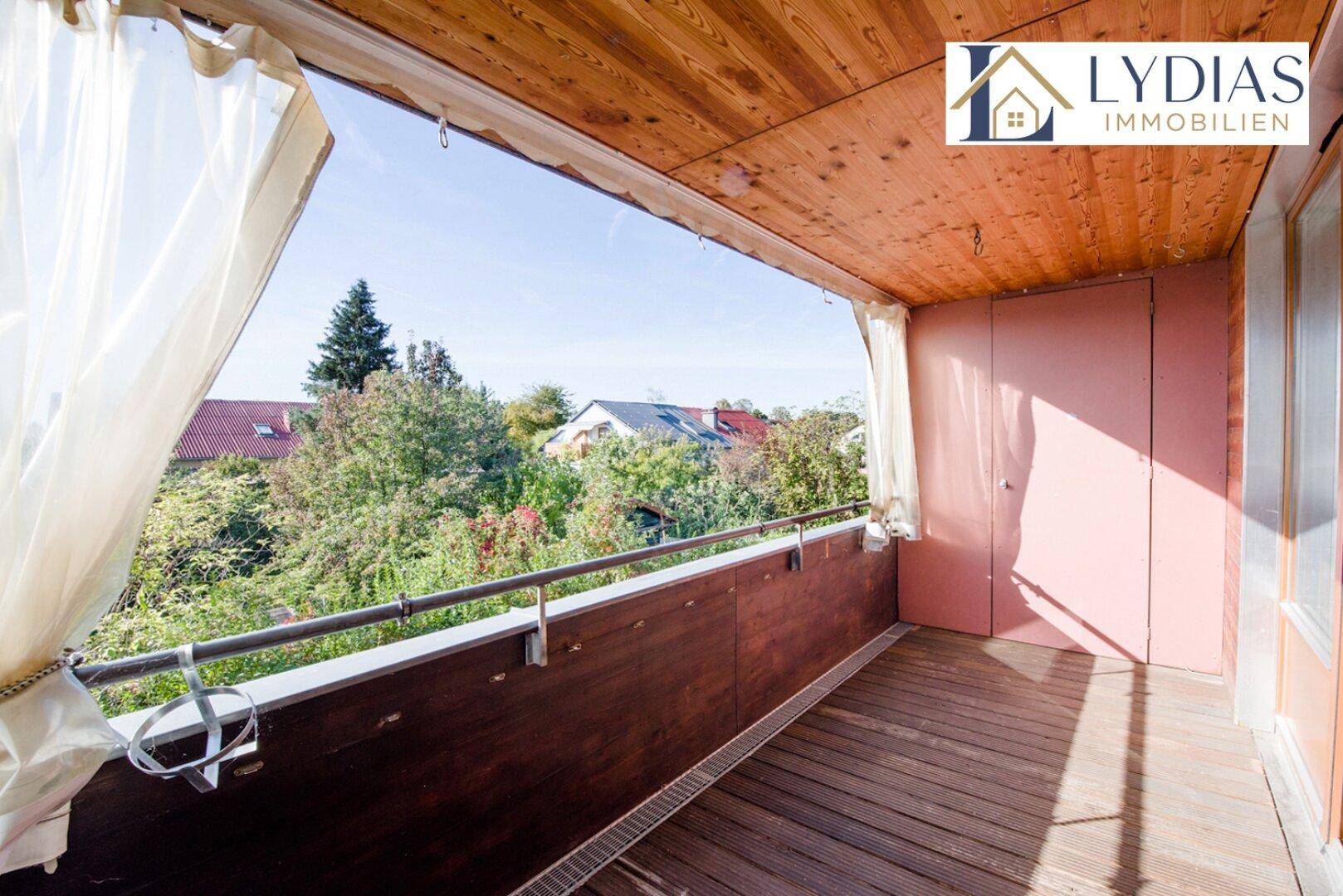 Überdachter Balkon mit Holzboden und Vorhängen, bietet Privatsphäre und einen Blick ins Grüne.