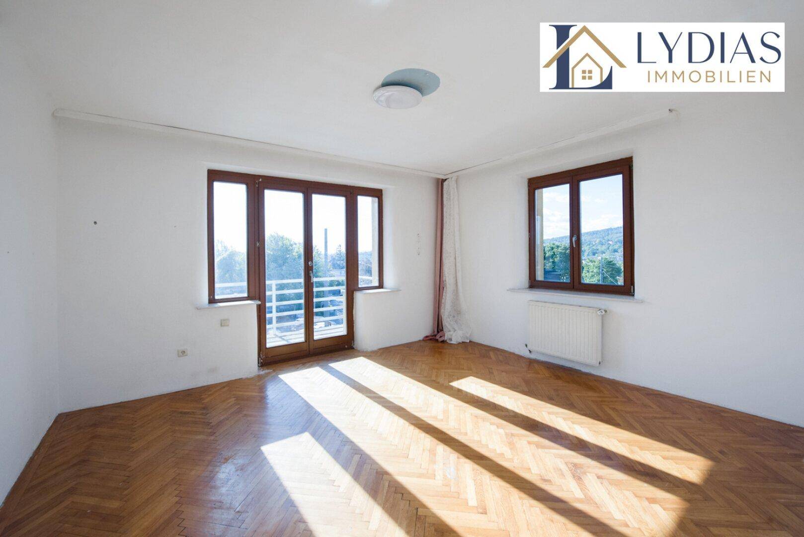 Helles Zimmer mit Fischgrätparkett und Zugang zu einem französischen Balkon.