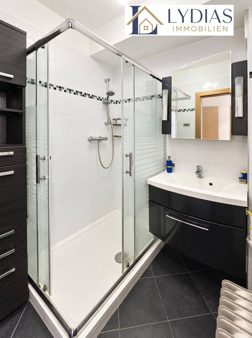 Modernes Badezimmer mit Duschkabine, dunklem Waschtischunterschrank und weißen Fliesen.