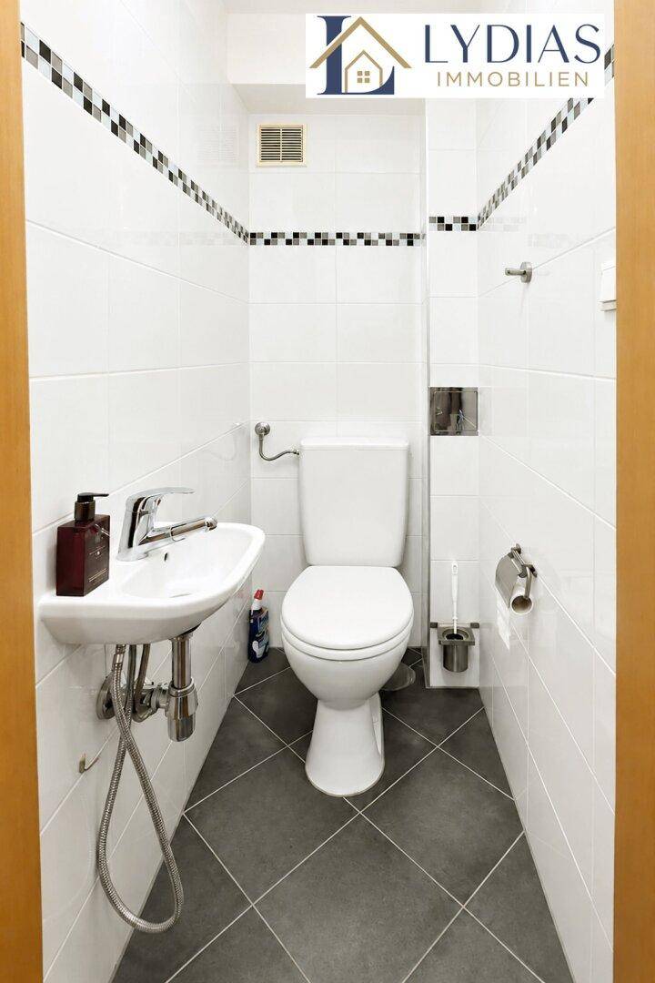 Kleines Gäste-WC mit wandmontiertem Waschbecken und Toilette, weiß gefliest und funktional.