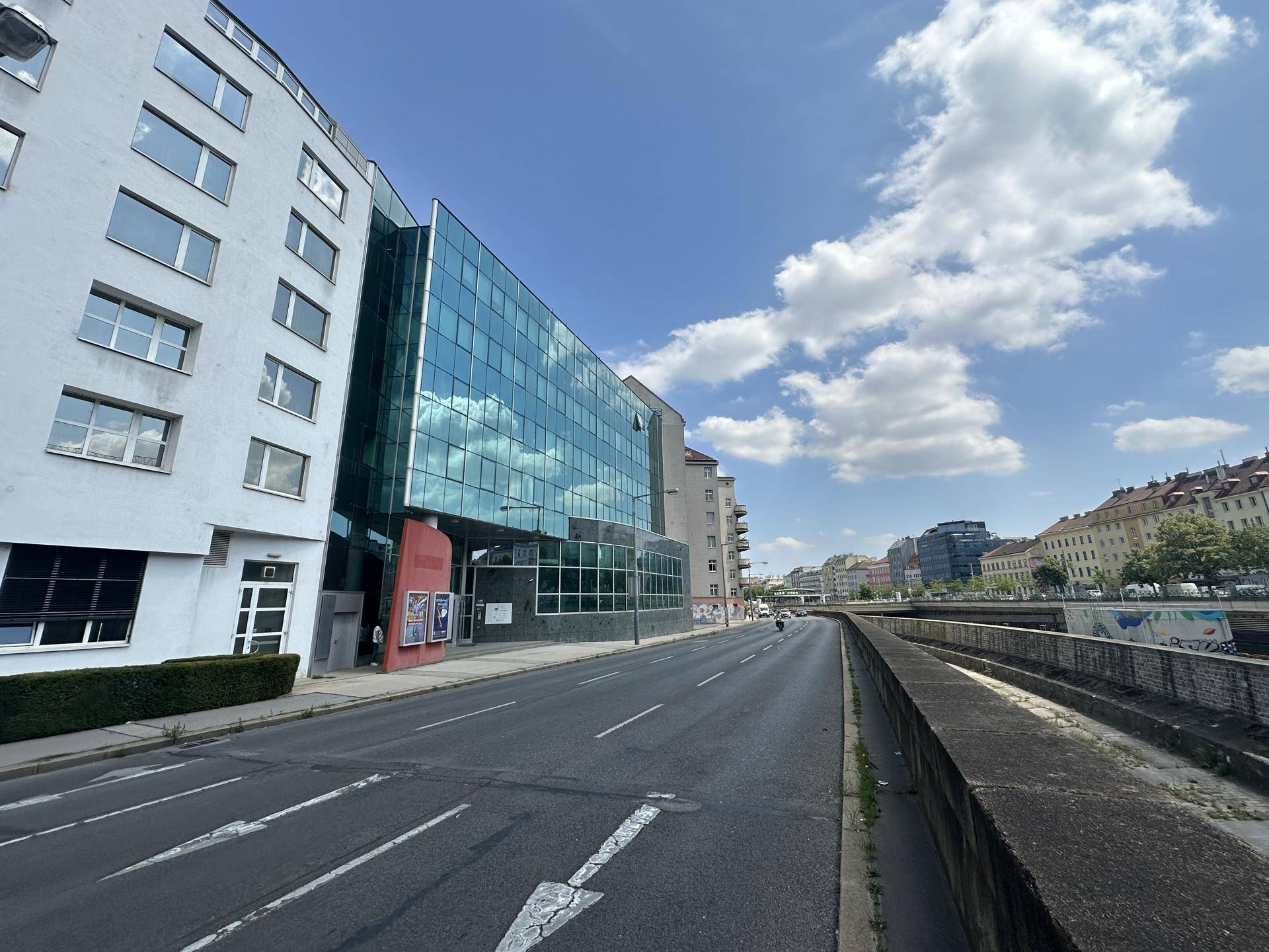 Weitwinkelansicht eines modernen Bürogebäudes mit Glasfassade entlang einer städtischen Straße.