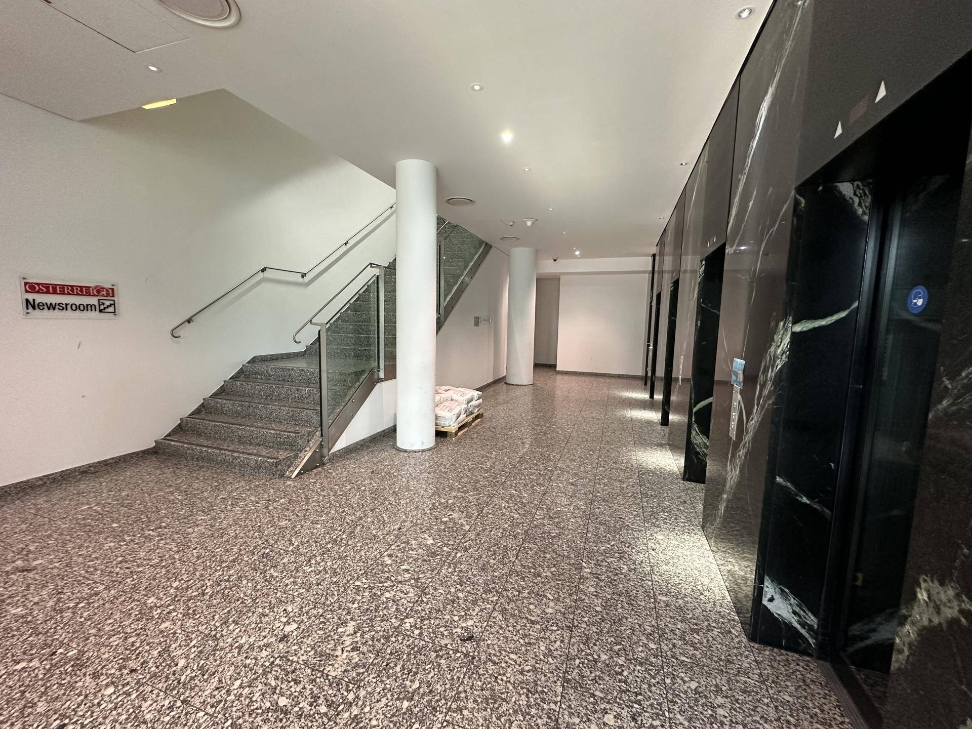 Geräumiger Eingangsbereich mit einer Treppe, Aufzügen mit Marmorverkleidung und einem Terrazzoboden.
