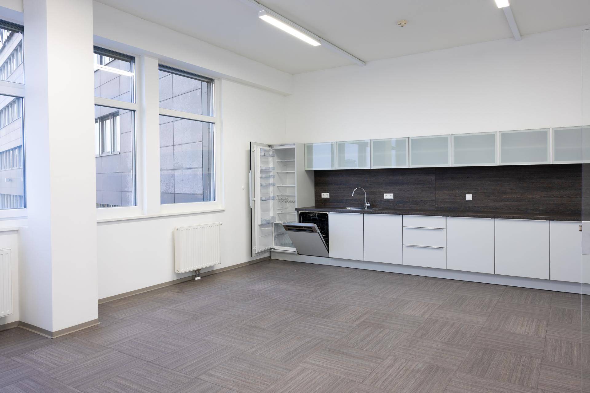 Moderne Büroküche mit weißen Schränken, dunkler Arbeitsplatte und integrierten Geräten.