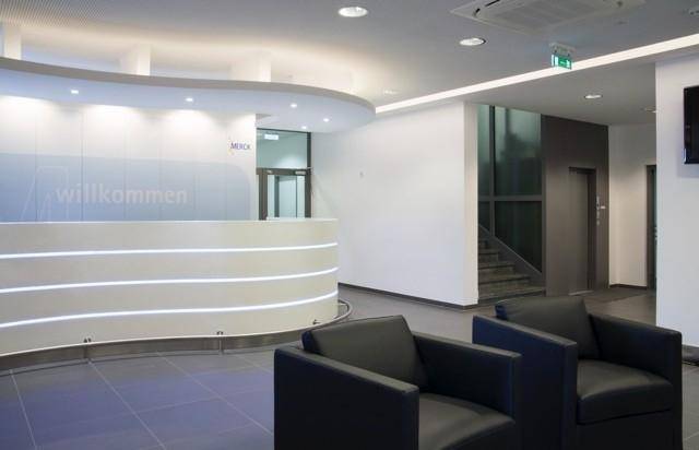 Moderner Empfangsbereich mit geschwungener Theke, bequemen schwarzen Sesseln und indirekter Beleuchtung.