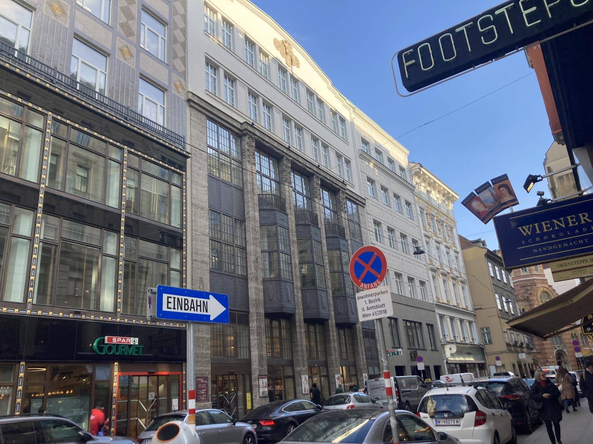 Belebte Stadtstraße mit historischen Gebäuden und Geschäften unter blauem Himmel.