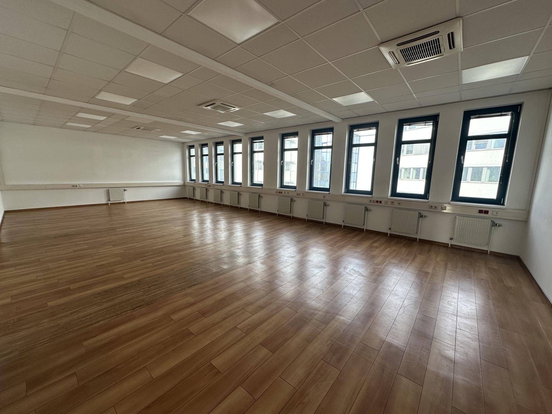 Geräumiger Büroraum mit Holzboden, vielen Fenstern und integrierter Deckenbeleuchtung.