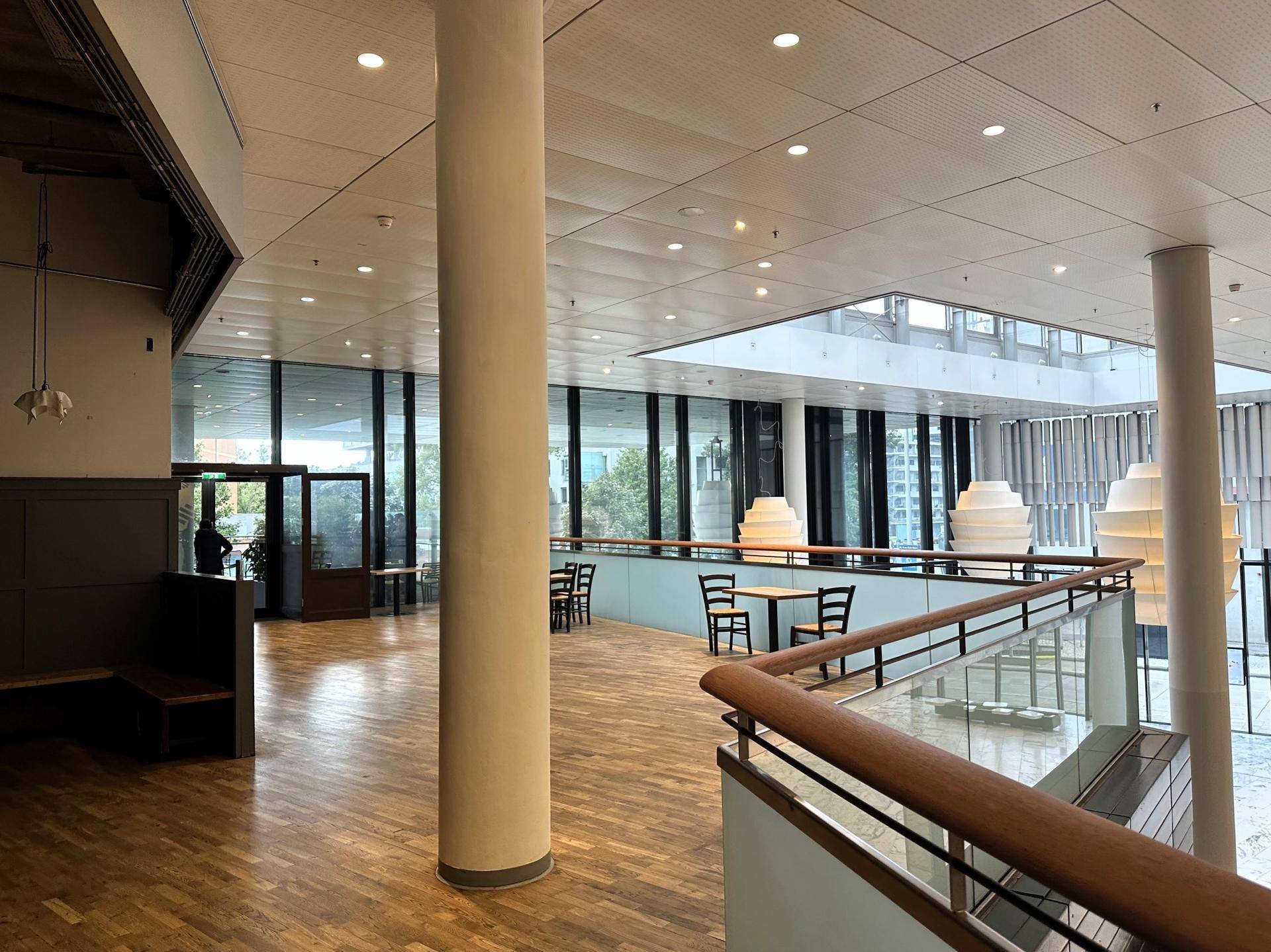 Übergangsbereich mit Holzboden und Blick auf die helle, moderne Lobby mit großen Fensterfronten.