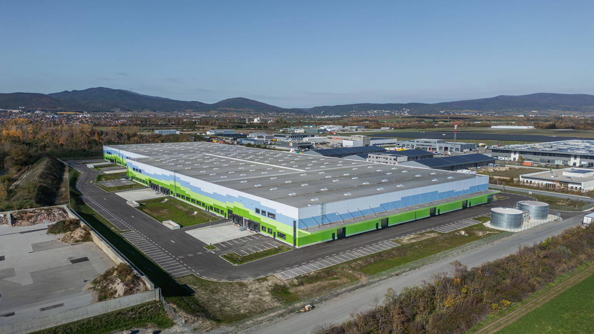 Weitläufiges Logistikzentrum mit farbiger Fassade und umliegendem Industriegebiet unter klarem Himmel.