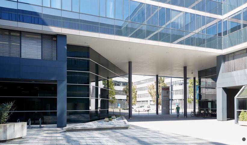 Eingangsbereich eines modernen Bürokomplexes mit überdachtem Vorplatz und Glasfronten.