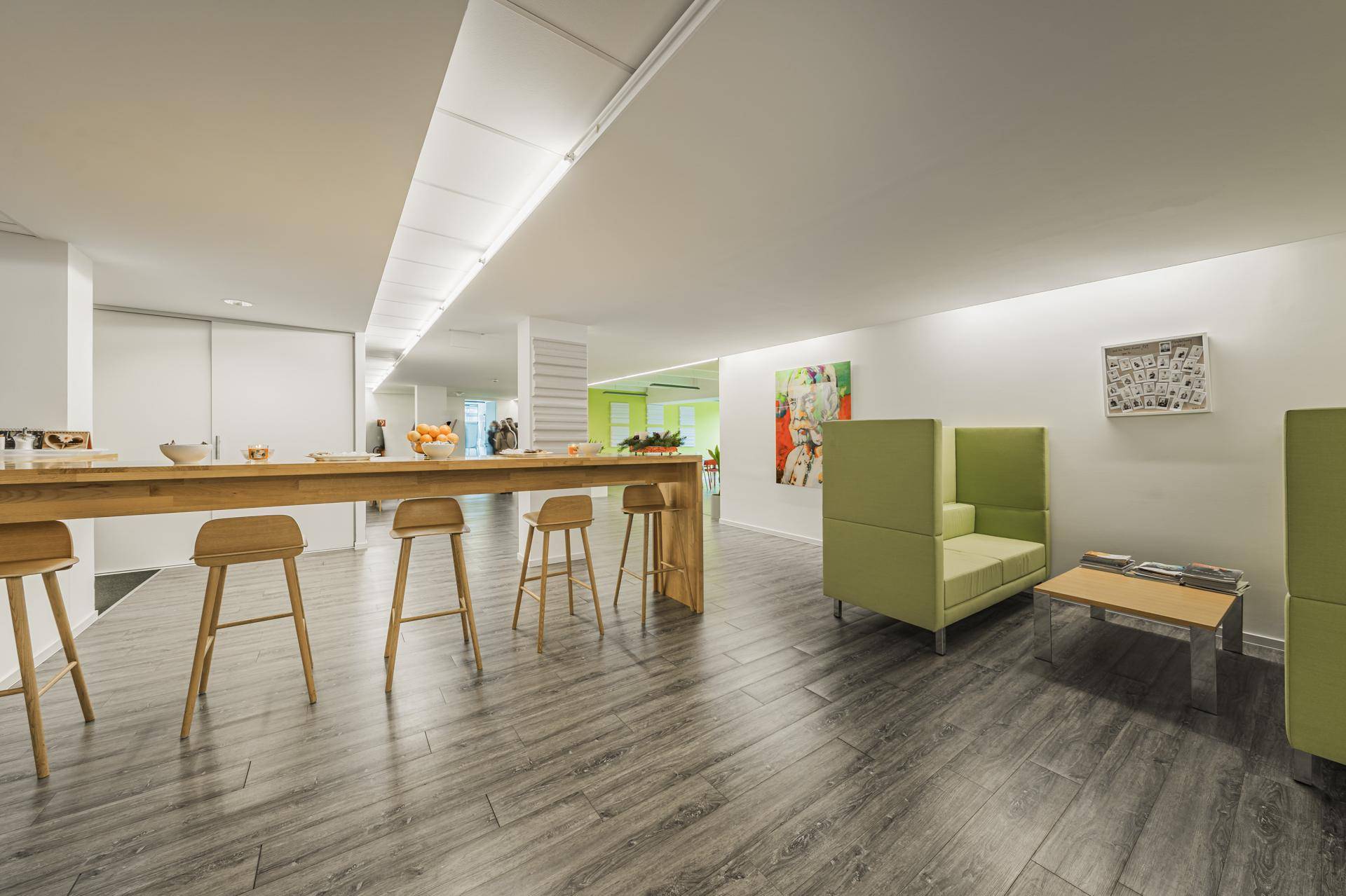 Moderner Loungebereich mit Holzboden, langen Holztischen und grünen Sitzmöbeln.