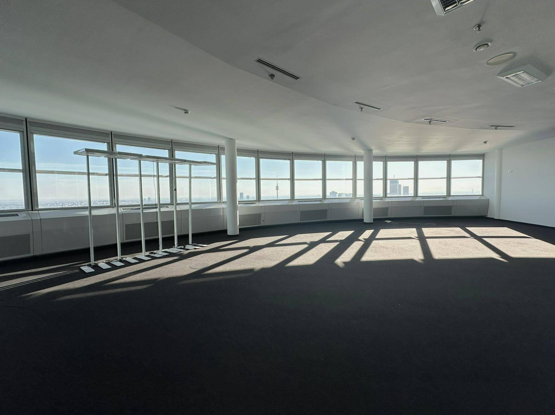 Großer, heller Büroraum mit dunklem Teppichboden und einer weiten Fensterfront, die einen Panoramablick bietet.