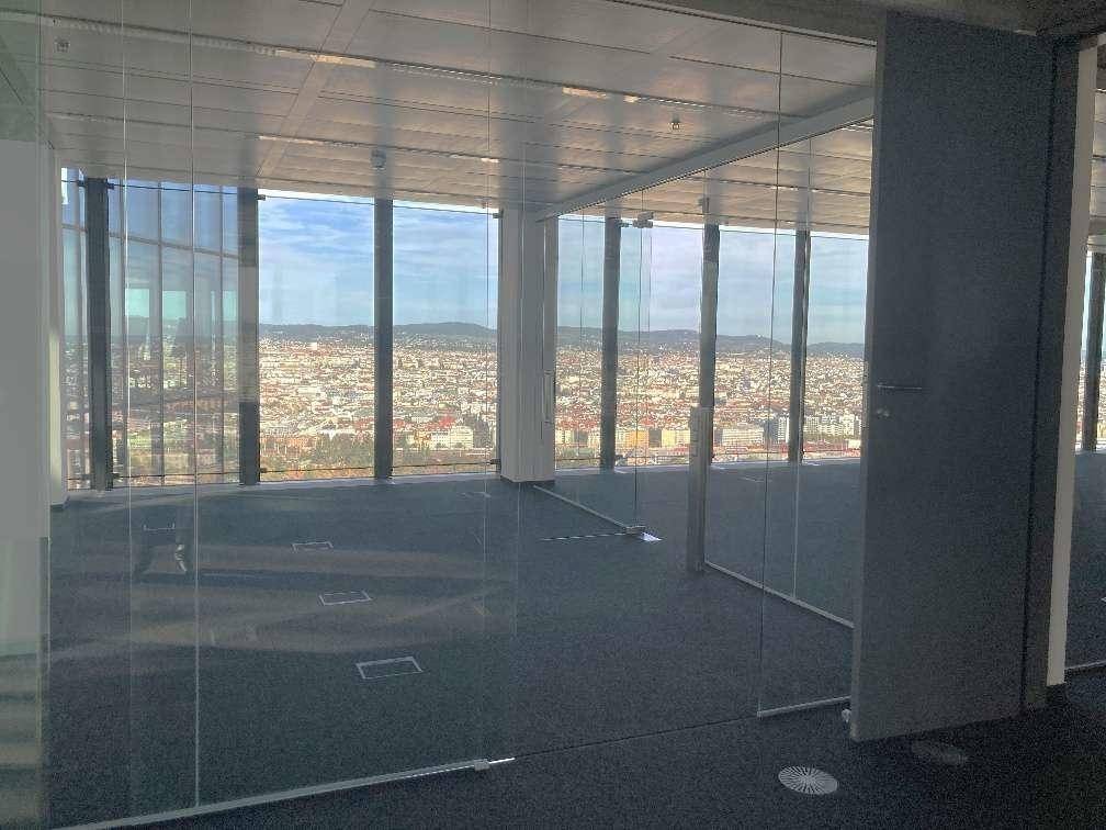 Heller, unmöblierter Büroraum mit Teppichboden, Glaswänden und weitem Blick über die Stadtlandschaft.