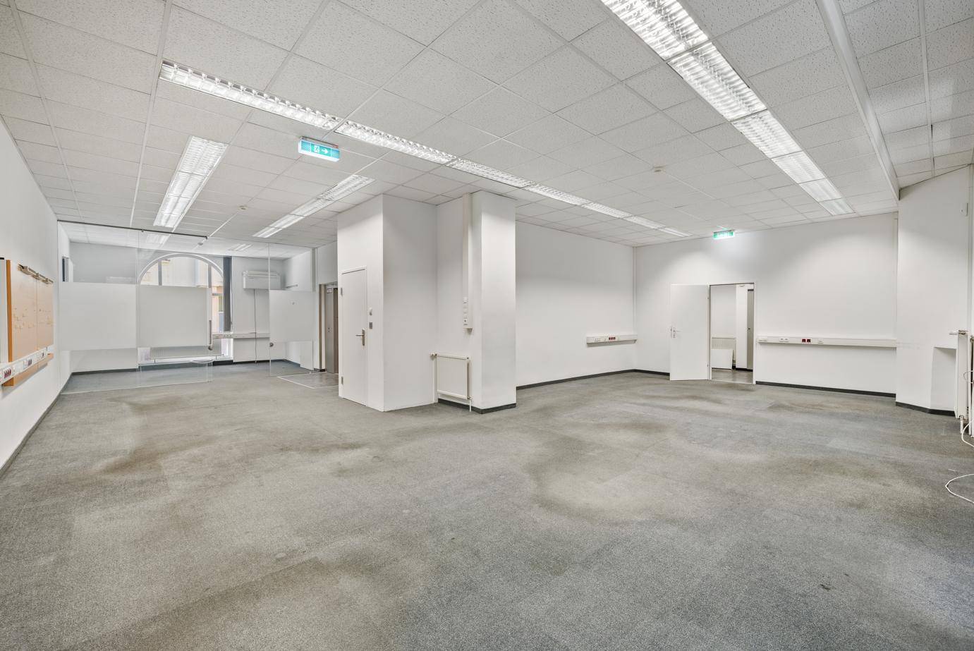 Großer, offener Bürobereich mit Teppichboden, Rasterdecke und mehreren Türen für Flexibilität.
