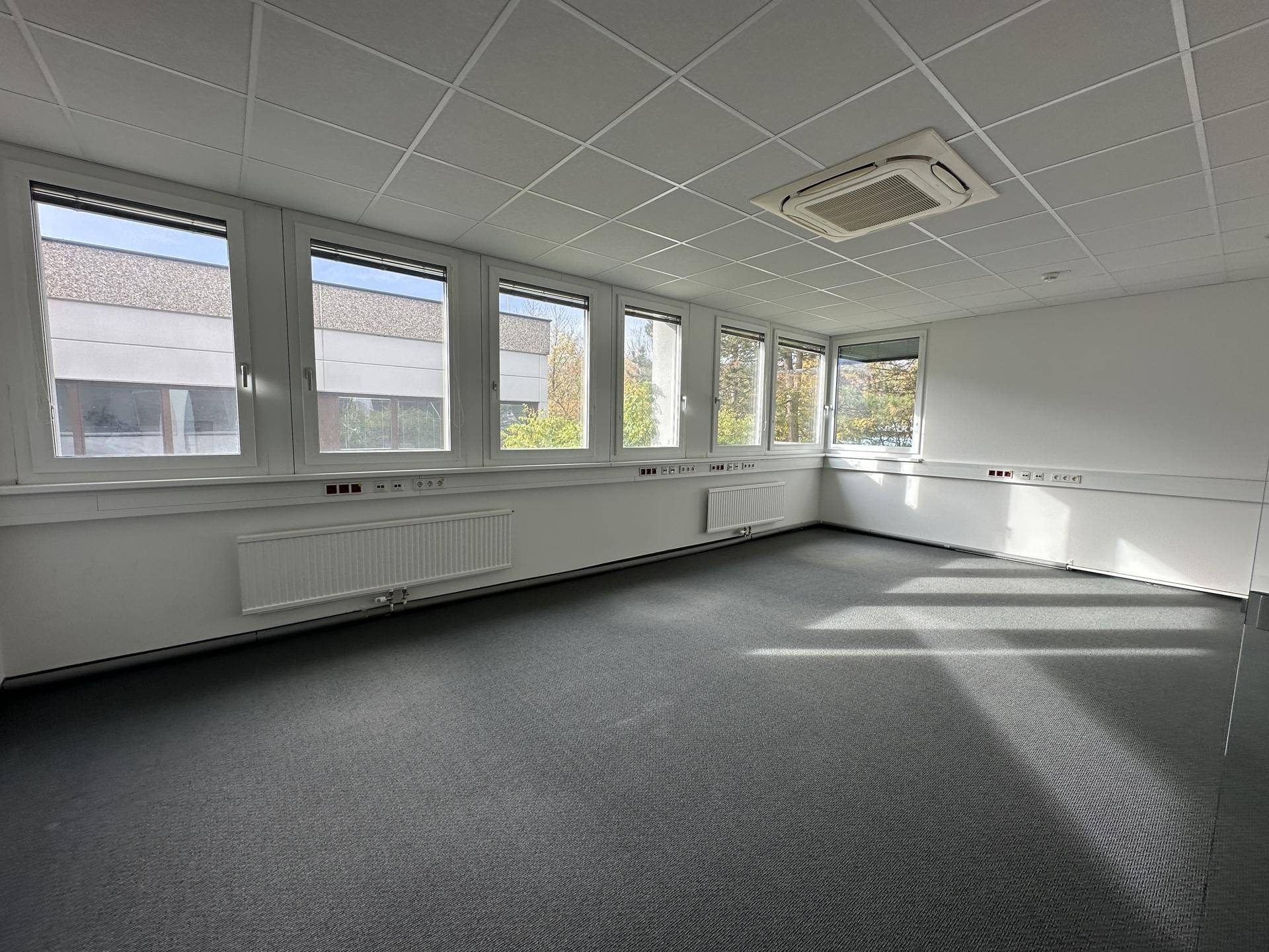 Helles Büro mit vielen Fenstern, Teppichboden und einer Klimaanlage an der Decke, ideal für Arbeitsplätze.