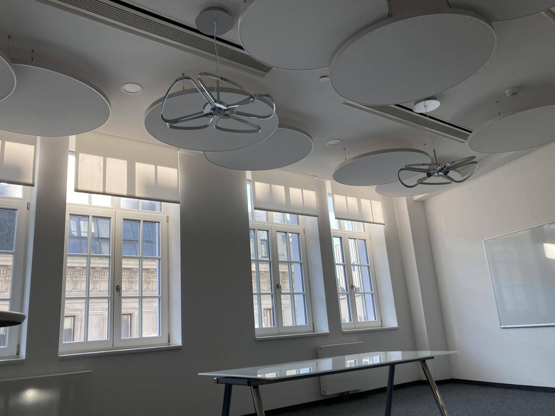 Konferenzraum mit großen Fenstern, Teppichboden und modernen, runden Deckenleuchten.