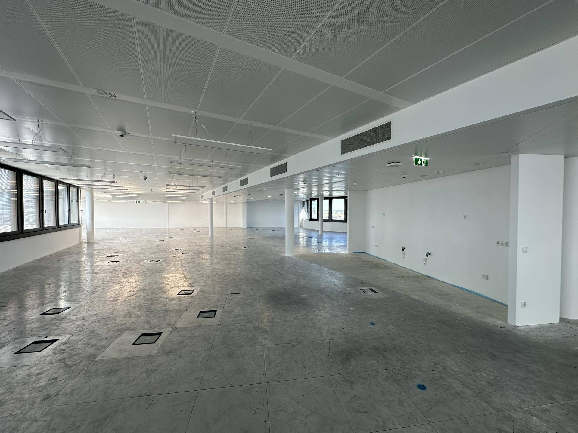 Weitläufiger, heller Bürobereich mit Bodentanks, Säulen und großen Fenstern, ideal für flexible Arbeitsplatzgestaltung.