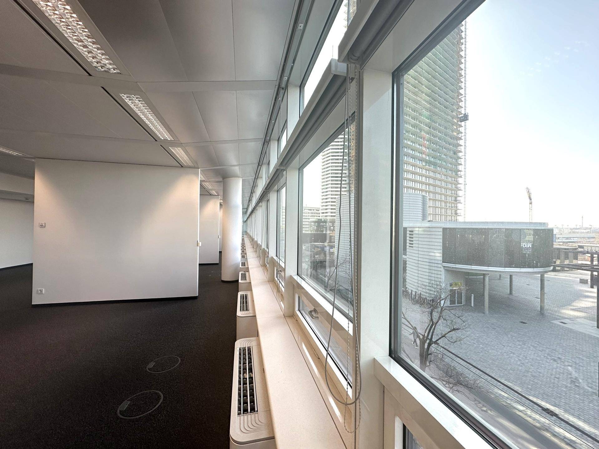 Langer Bürogang mit durchgehenden Fenstern und Blick auf die umliegenden Gebäude.