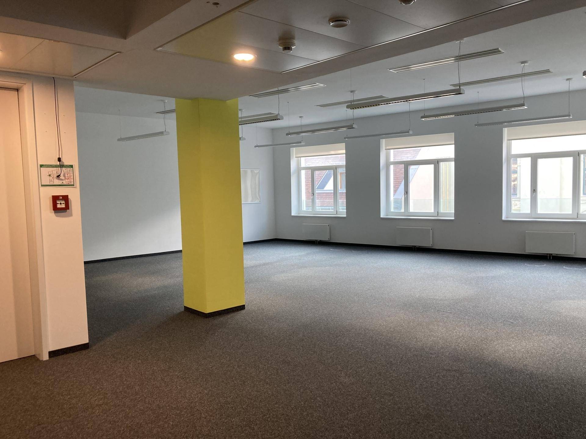 Leeres Büro mit Teppichboden, einem gelben Pfeiler und großen Fenstern für Tageslicht.