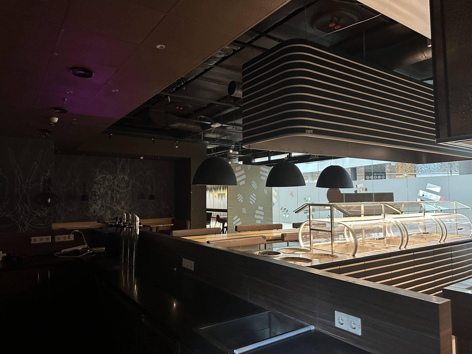 Servicetheke des Restaurants mit integrierten Vitrinen und modernen schwarzen Pendelleuchten unter einer stilvollen Decke.