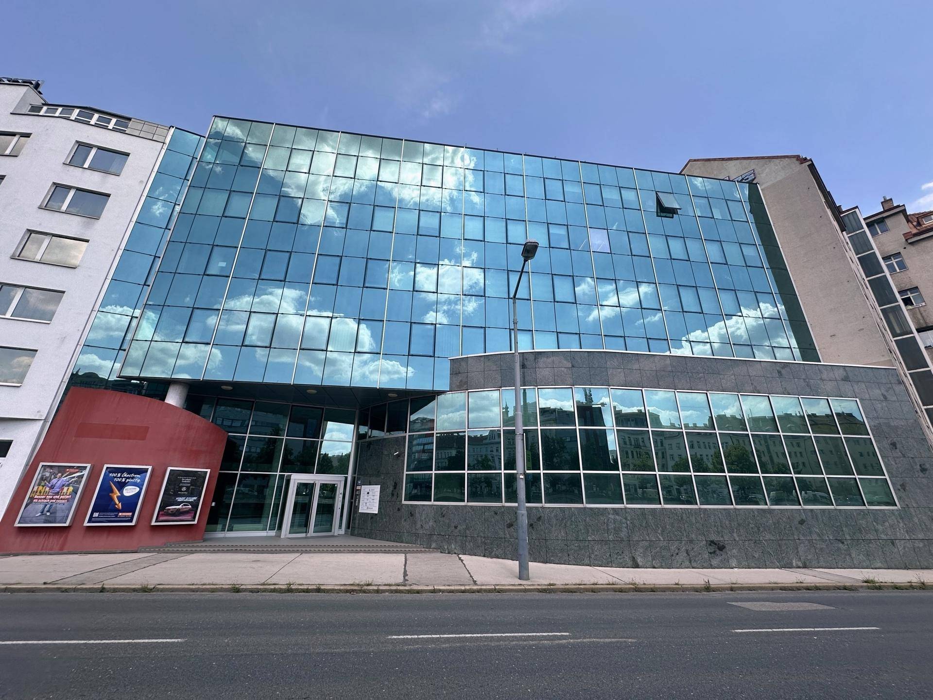 Ansicht eines modernen Bürogebäudes mit markanter Glasfassade und reflektierendem Himmel an einer Straße.