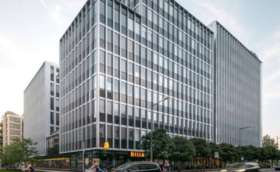 Zeitgenössisches Bürogebäude mit vertikalen Fensterbändern und einer belebten Straße davor.