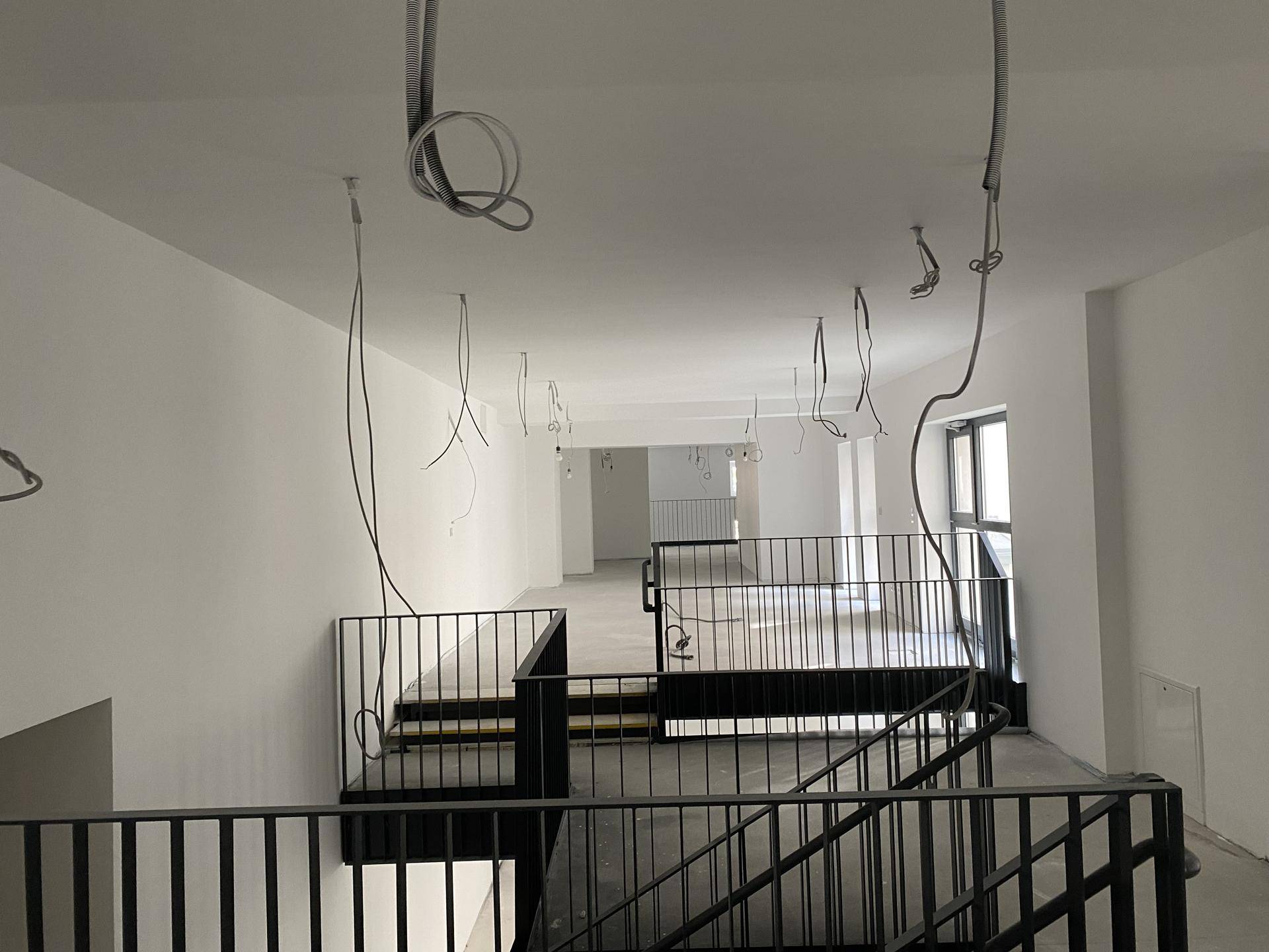 Blick von einer oberen Ebene auf das schwarze Metallgeländer und die Treppe in einem offenen Innenraum.