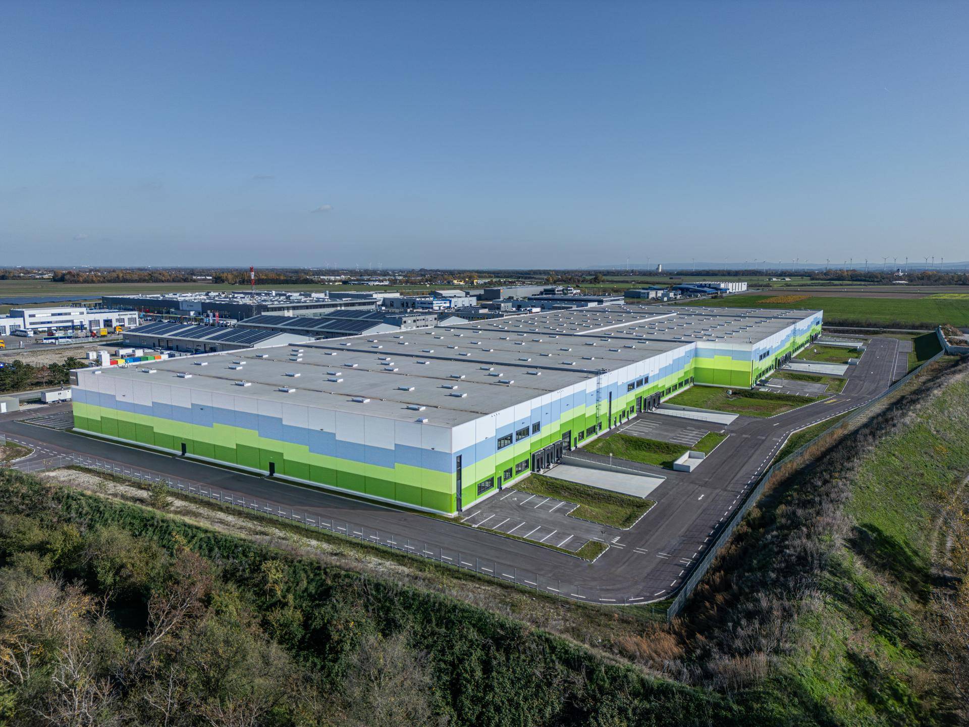 Panoramablick aus der Luft auf den modernen Industriepark mit weitläufigen Lagerhallen und angrenzenden Feldern.