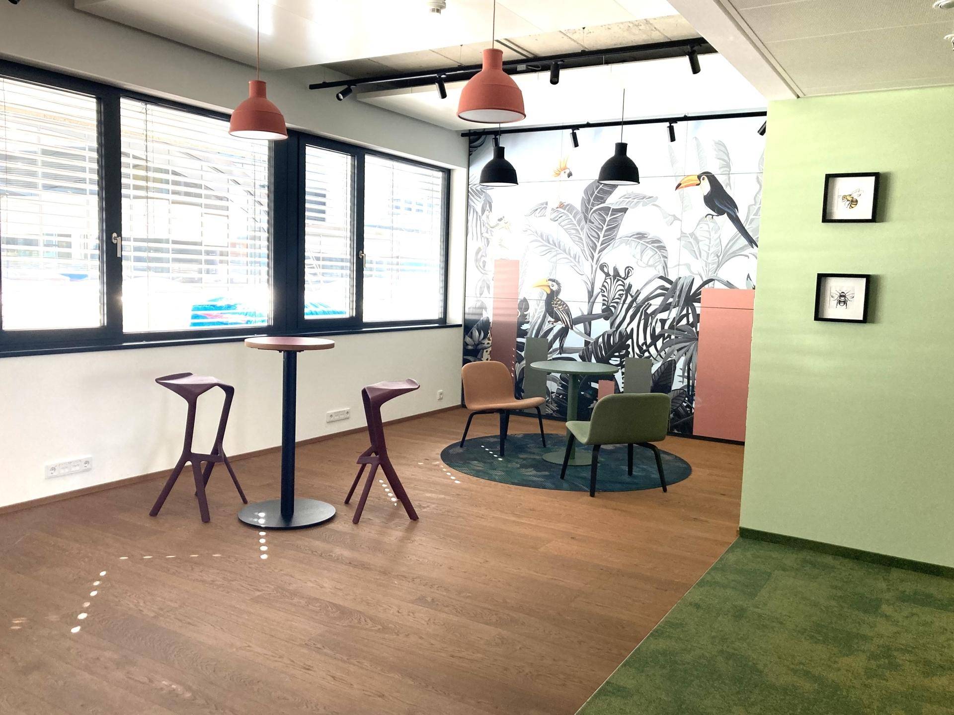 Farbenfroher Bürobereich mit Wandgemälde, modernen Möbeln und Holzboden nahe den großen Fenstern.