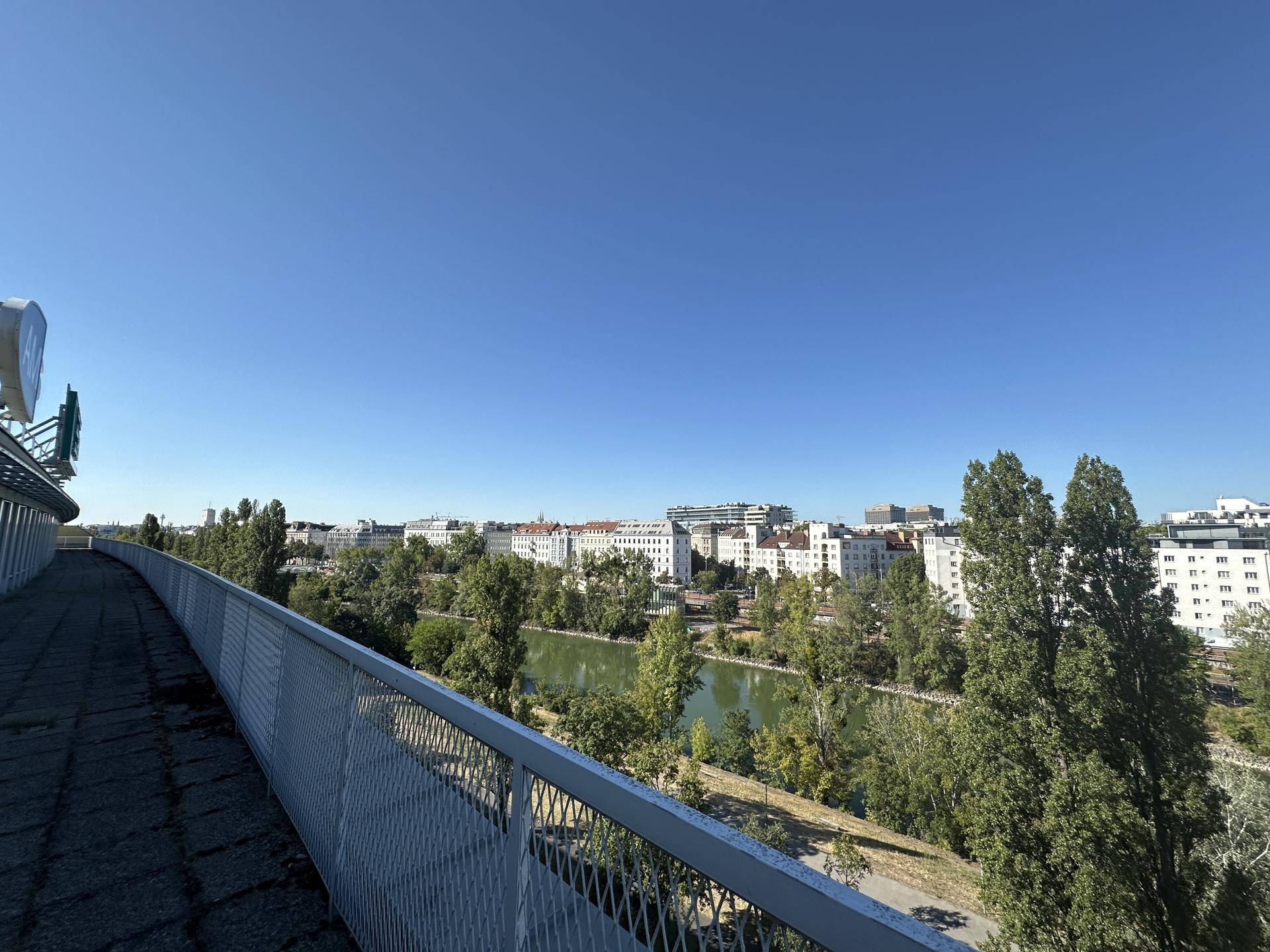 Panoramablick von einem erhöhten Gang auf die Stadt, den Fluss und die grüne Umgebung unter blauem Himmel.