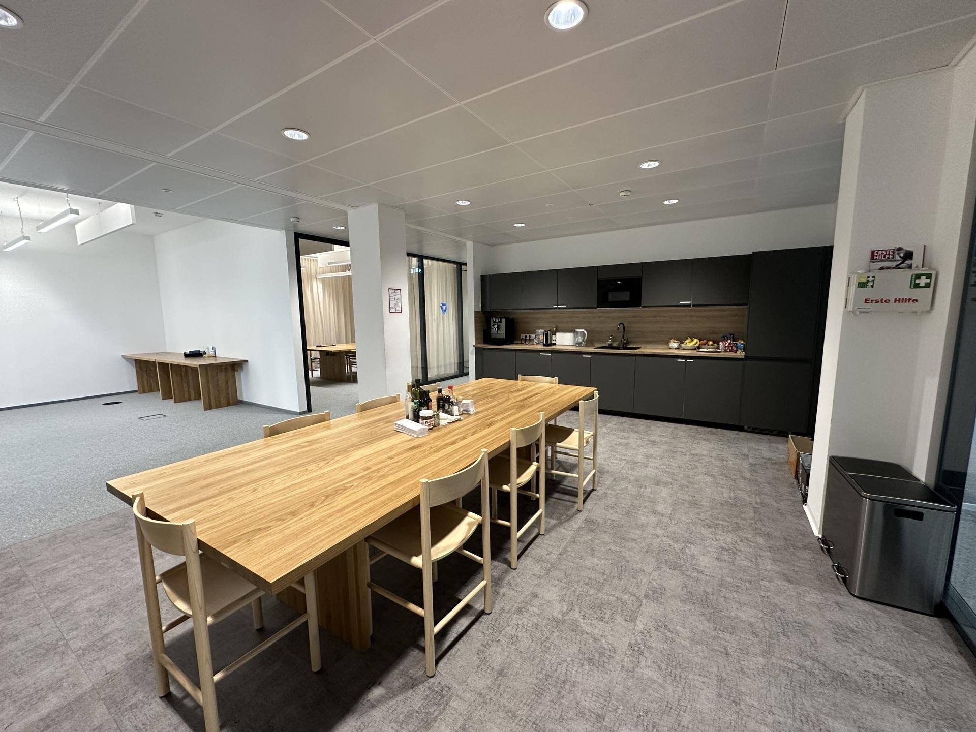 Geräumiger Küchen- und Essbereich mit dunkler Einbauküche und großem Holztisch, ideal für Pausen.