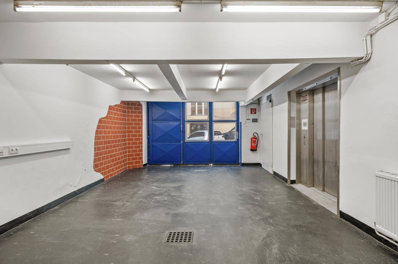 Eingangsbereich mit Betonboden, blauer Doppeltür und Aufzug.