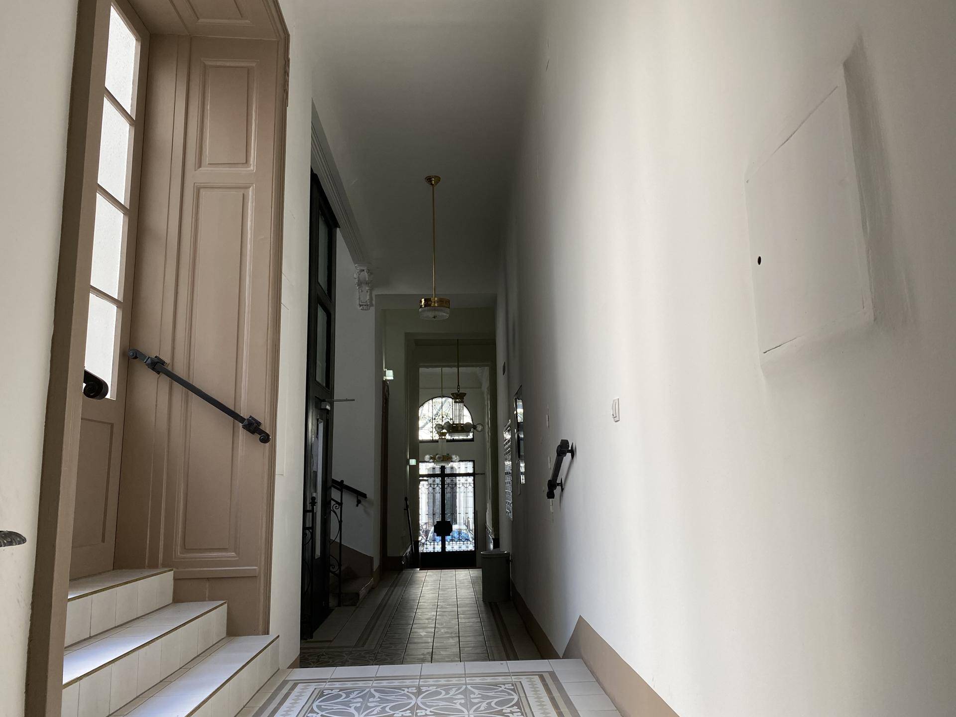 Langer Flur oder Eingangsbereich mit gemustertem Fliesenboden und einer Treppe in einem Altbau.