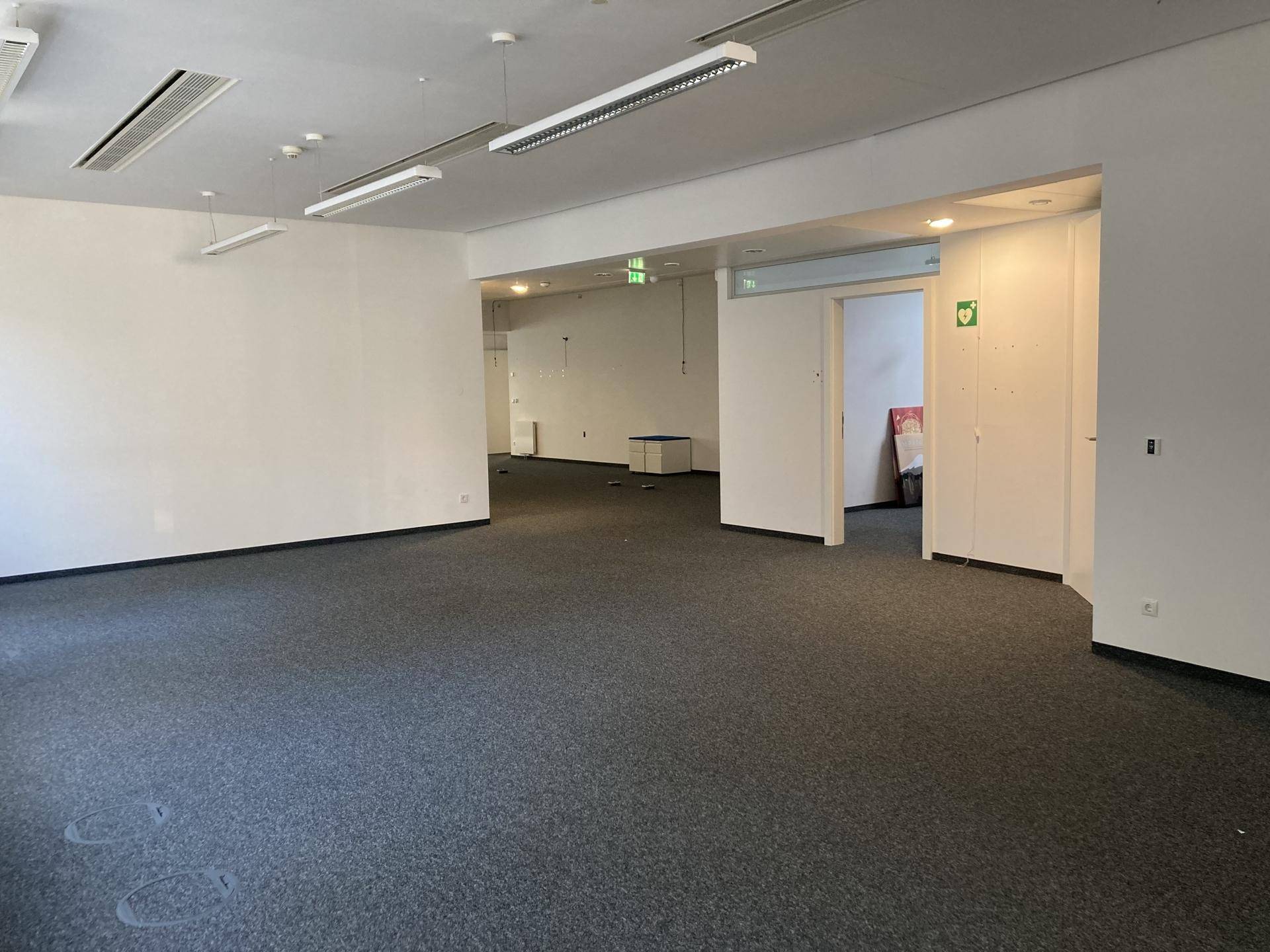 Großes, leeres Büro mit Teppichboden und offenen Durchgängen zu weiteren Bereichen.