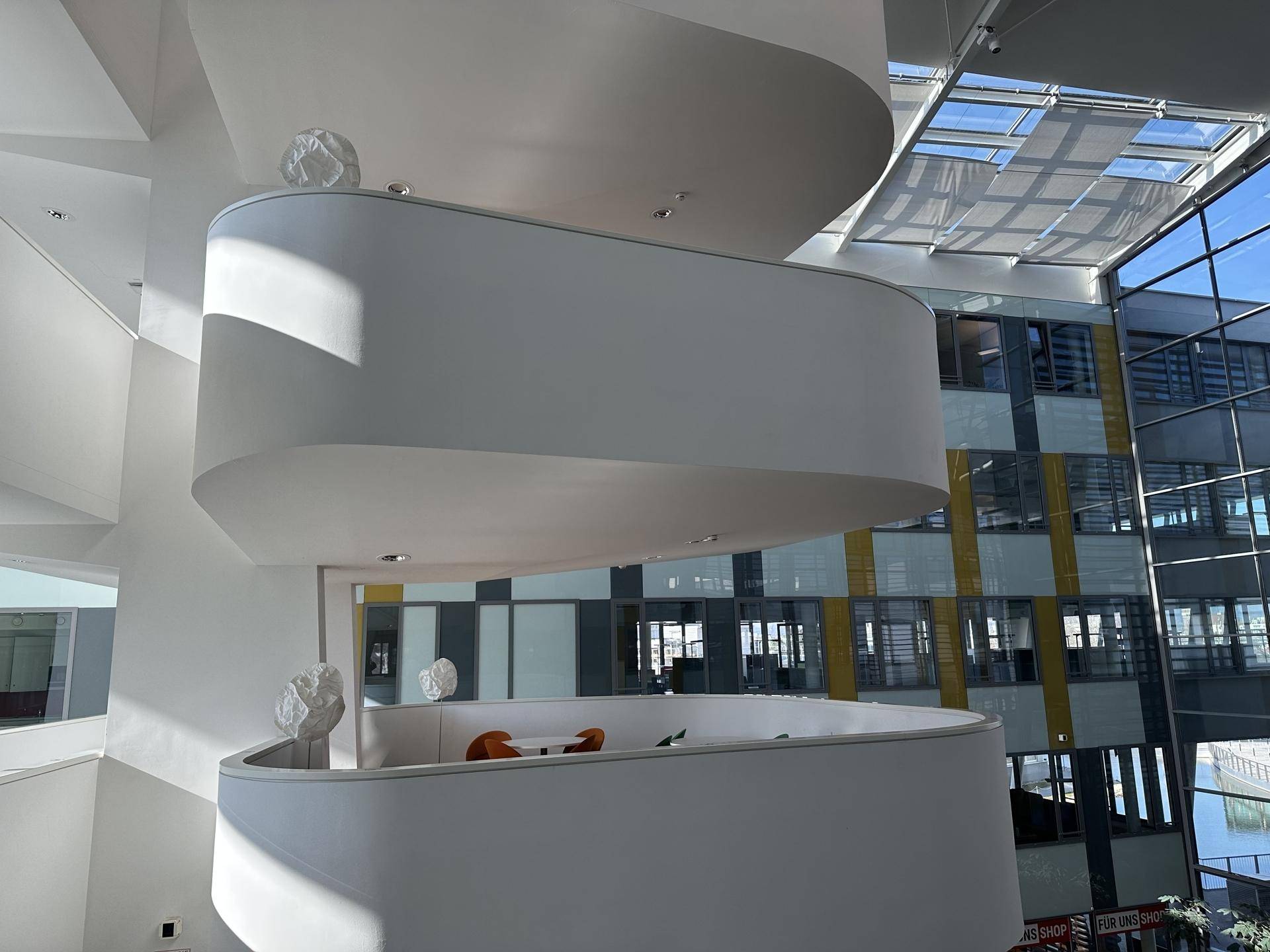 Geschwungene, mehrstöckige Lounge-Bereiche in einem modernen Gebäude mit viel Tageslicht und offener Architektur.