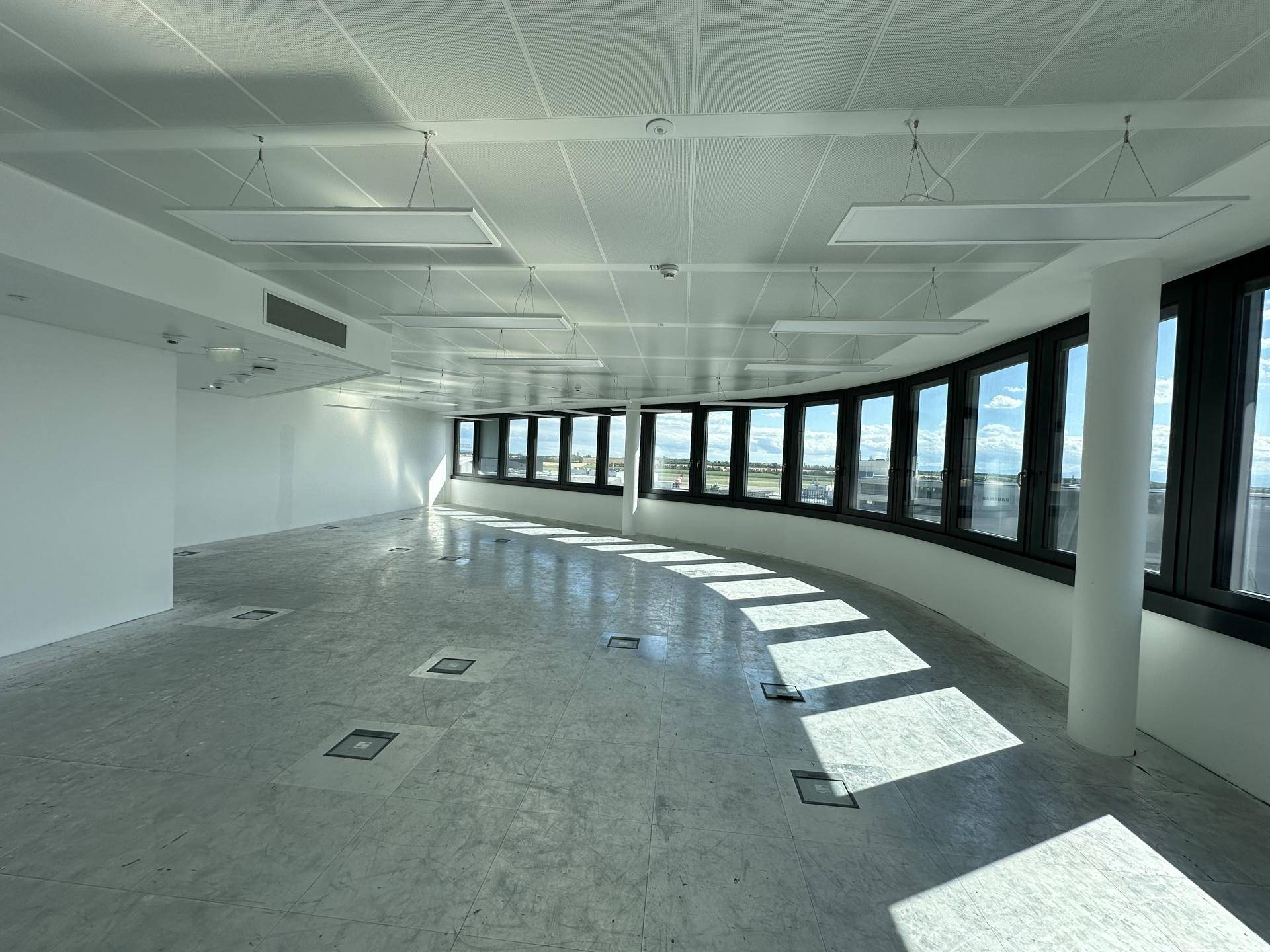 Heller, weitläufiger Bürobereich mit geschwungener Fensterfront, Bodentanks und abgehängter Decke.