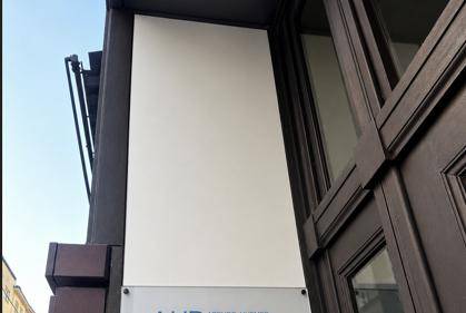 Detailansicht der Gebäudefassade mit einem Schild und dunklen Fensterrahmen.