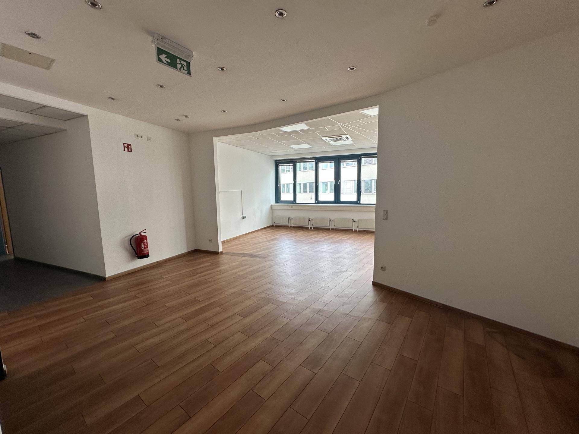 Heller Büroraum mit Holzboden und großen Fenstern, die viel Tageslicht hereinlassen.