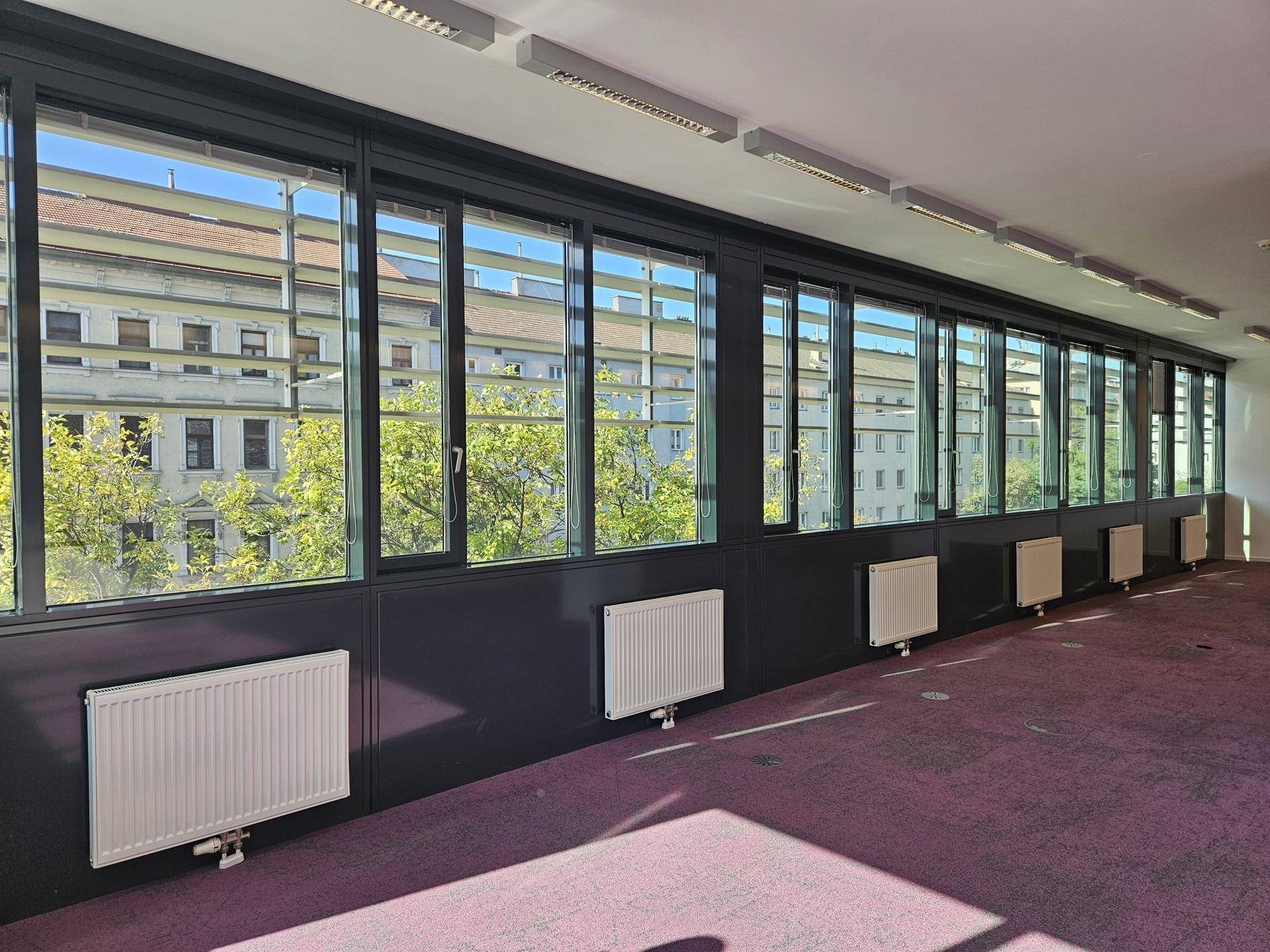 Langer Bürobereich mit durchgehender Fensterfront, die viel Tageslicht hereinlässt und Stadtblick bietet.
