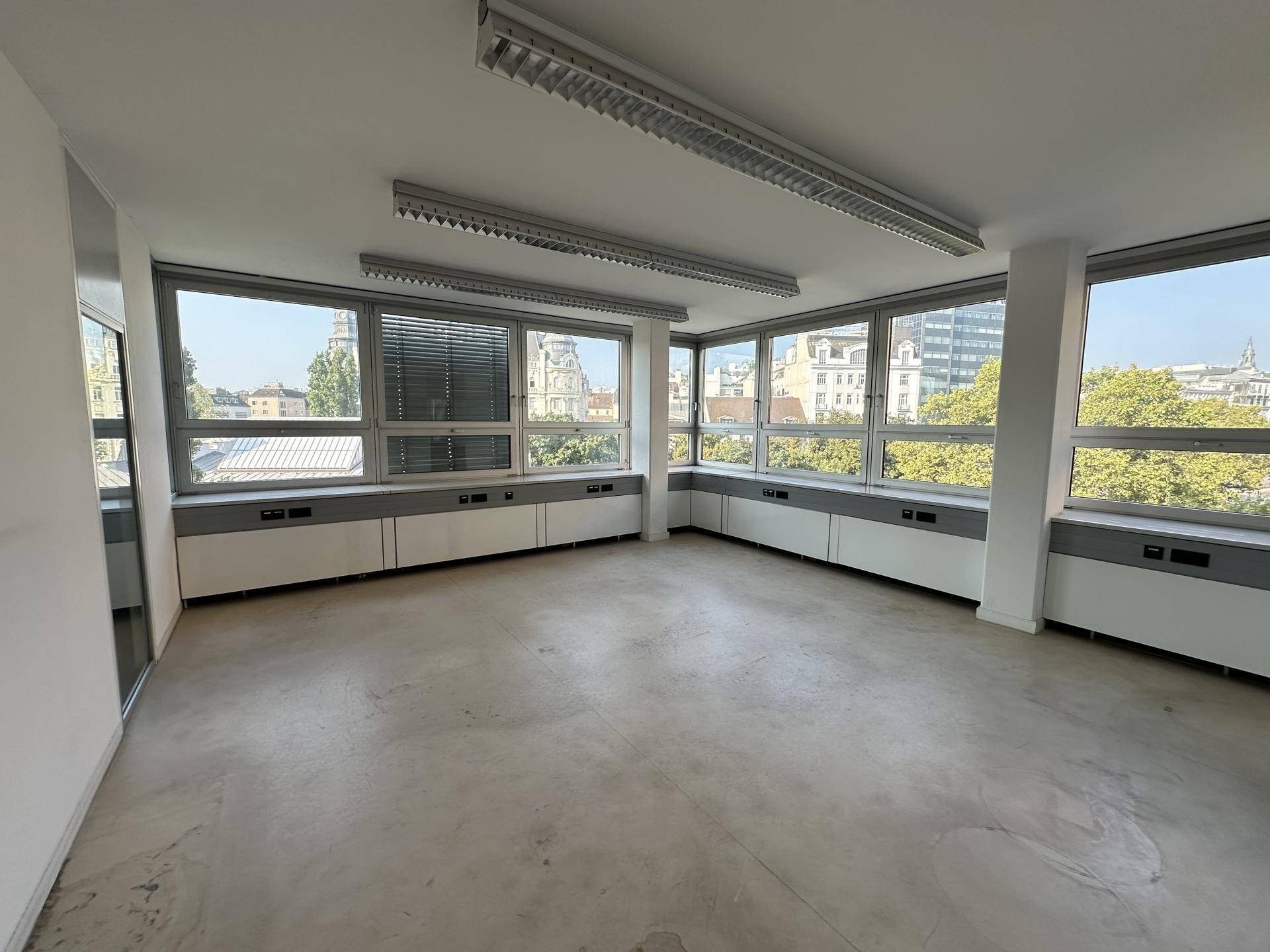 Leerer Büroraum mit großen Fenstern, die eine weite Aussicht bieten, und einem modernen Betonboden.