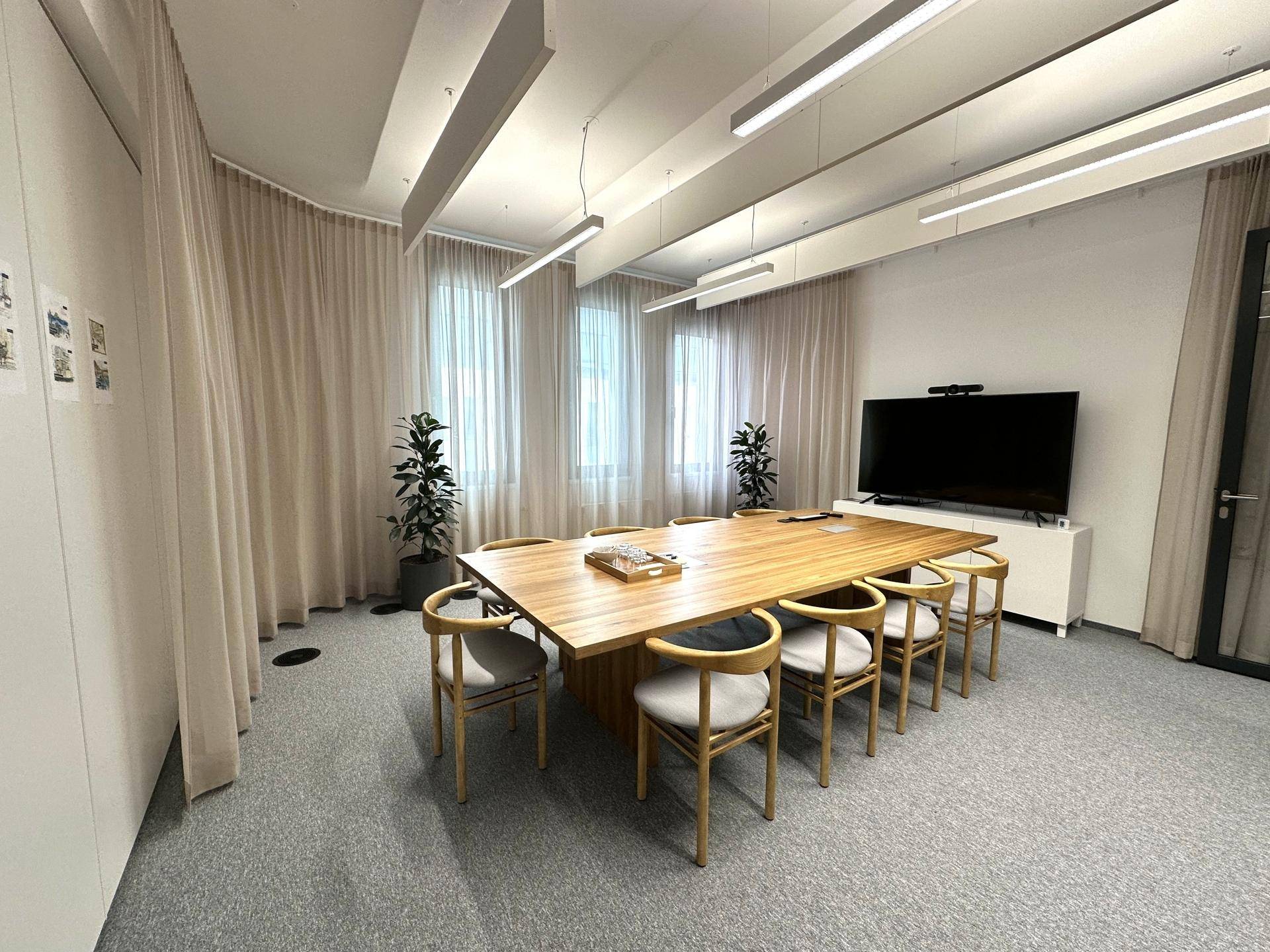 Großer Konferenzraum mit langem Holztisch, bequemen Stühlen und einem großen Bildschirm für Präsentationen.