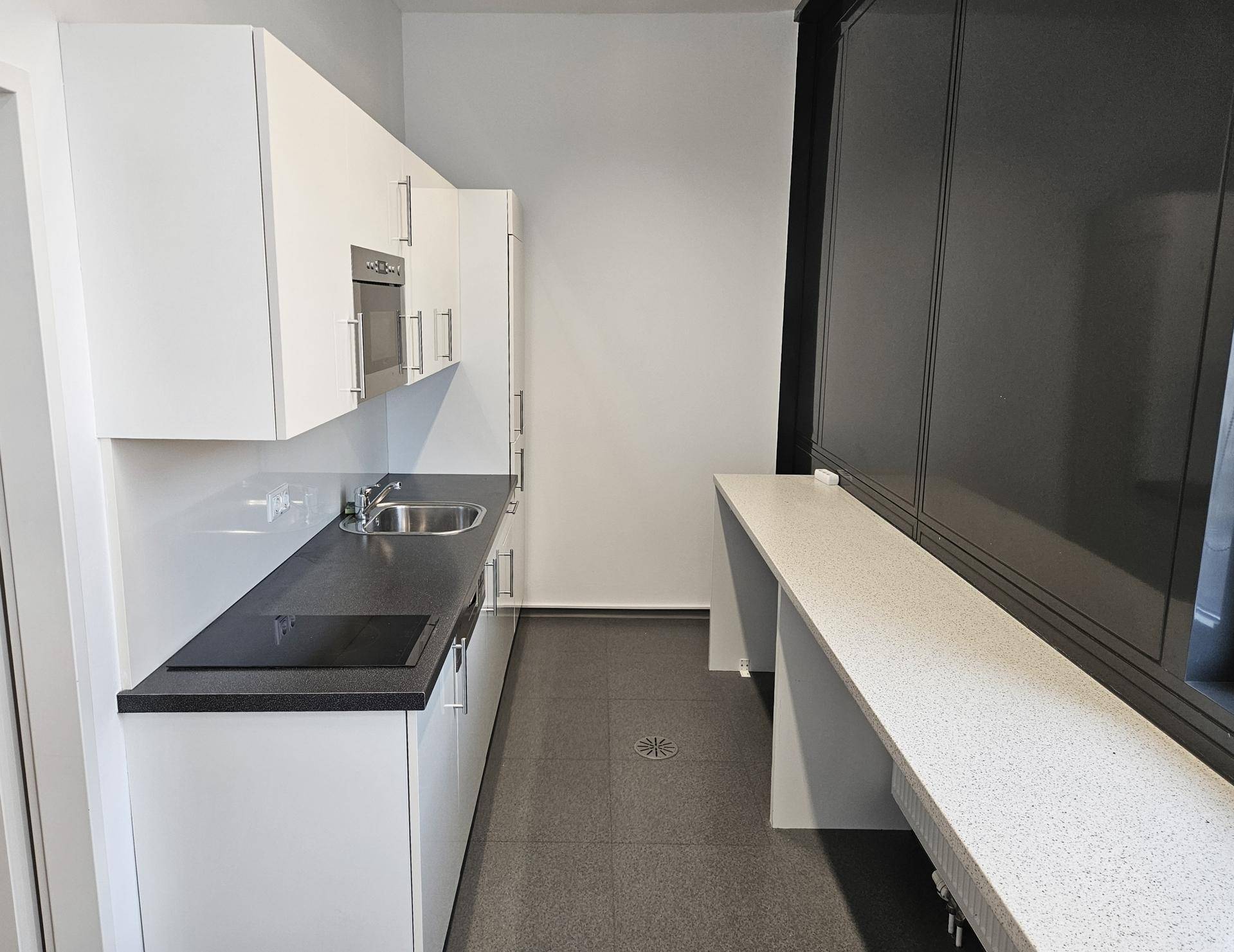 Moderne weiße Einbauküche mit dunkler Arbeitsplatte, integrierten Geräten und Fliesenboden in einem hellen Raum.