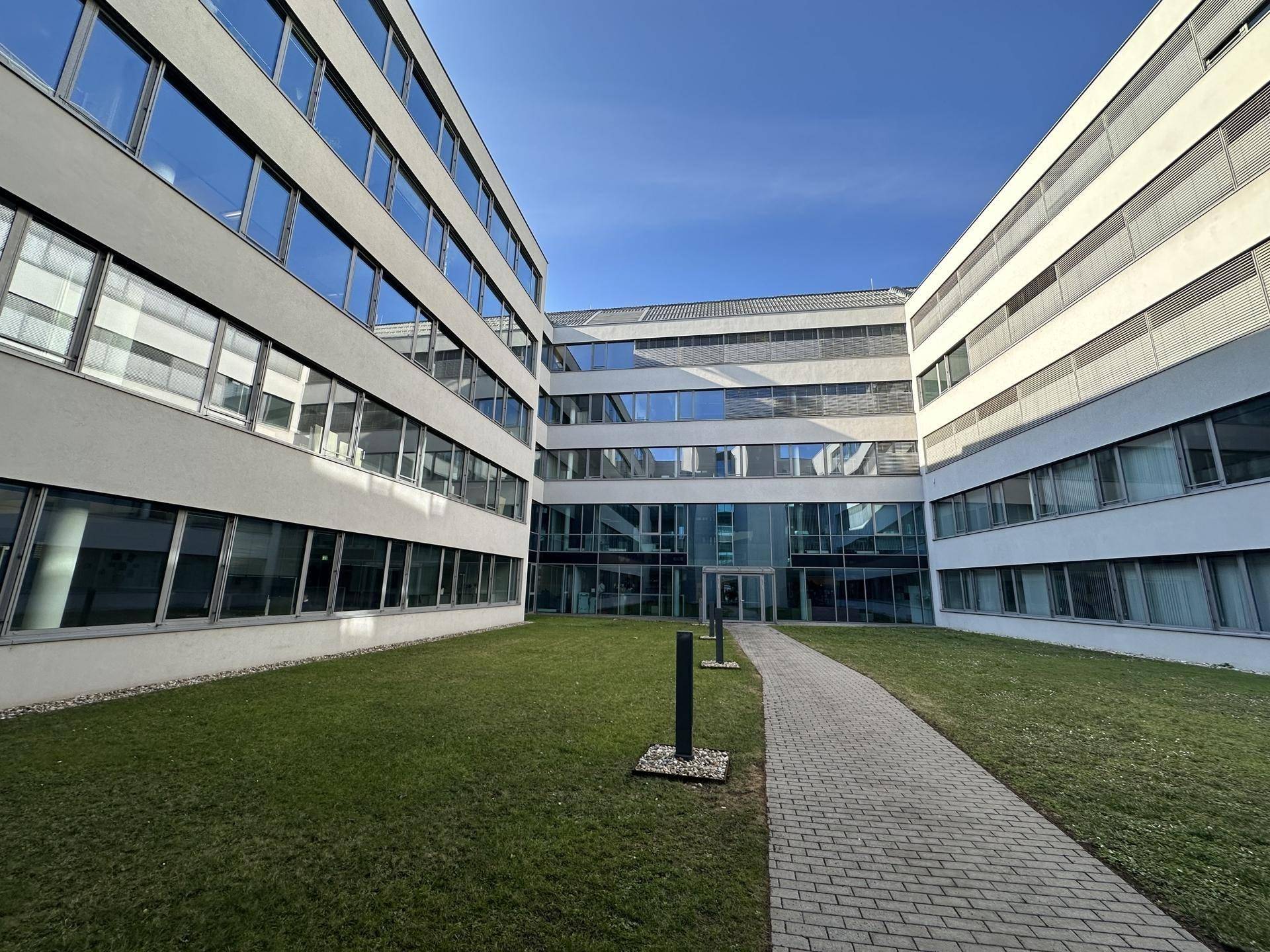 Innenhof eines modernen Bürokomplexes mit Rasenfläche und gepflastertem Weg.