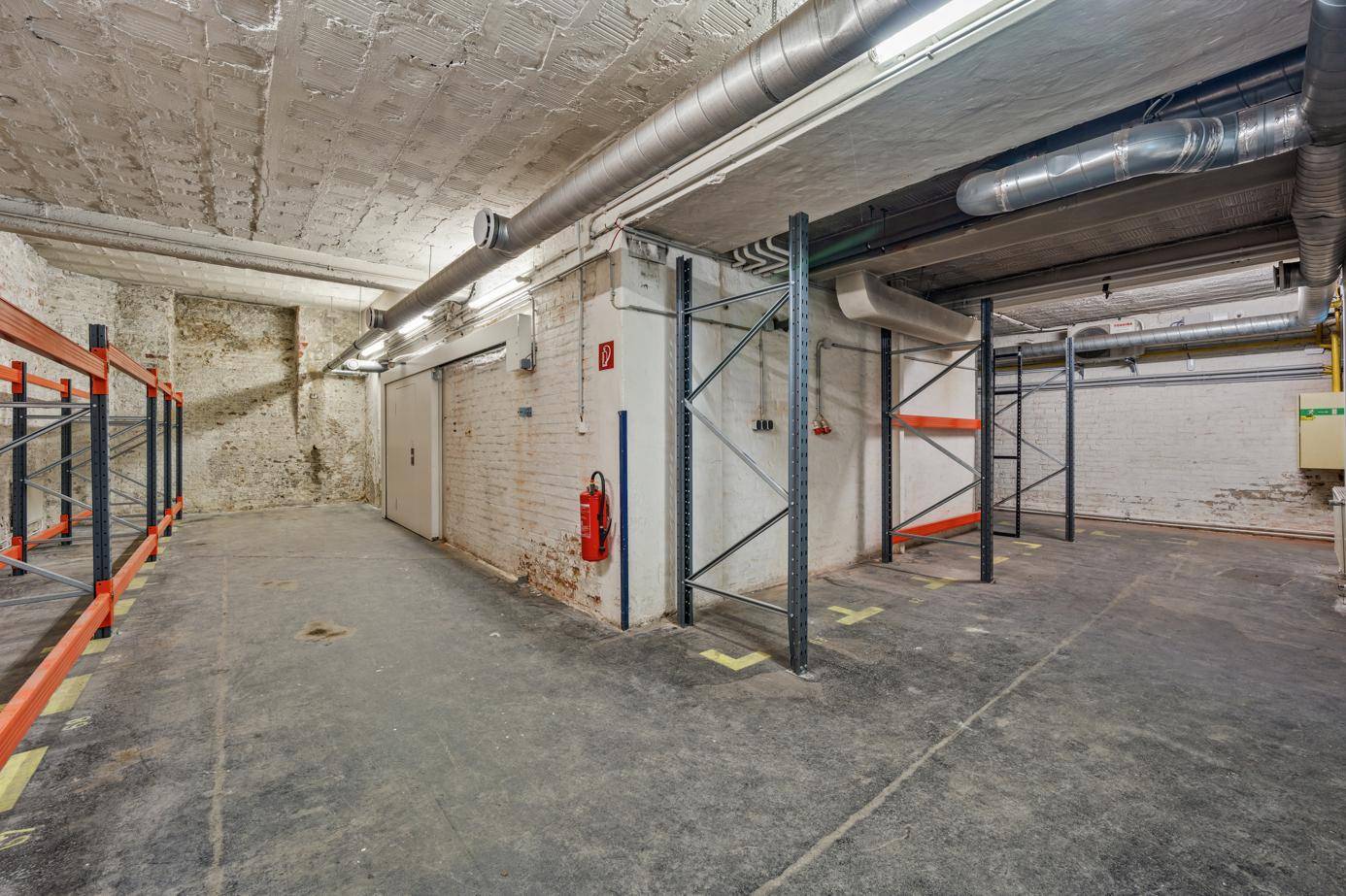 Lagerraum mit Betonboden, sichtbaren Rohren und Regalsystemen.