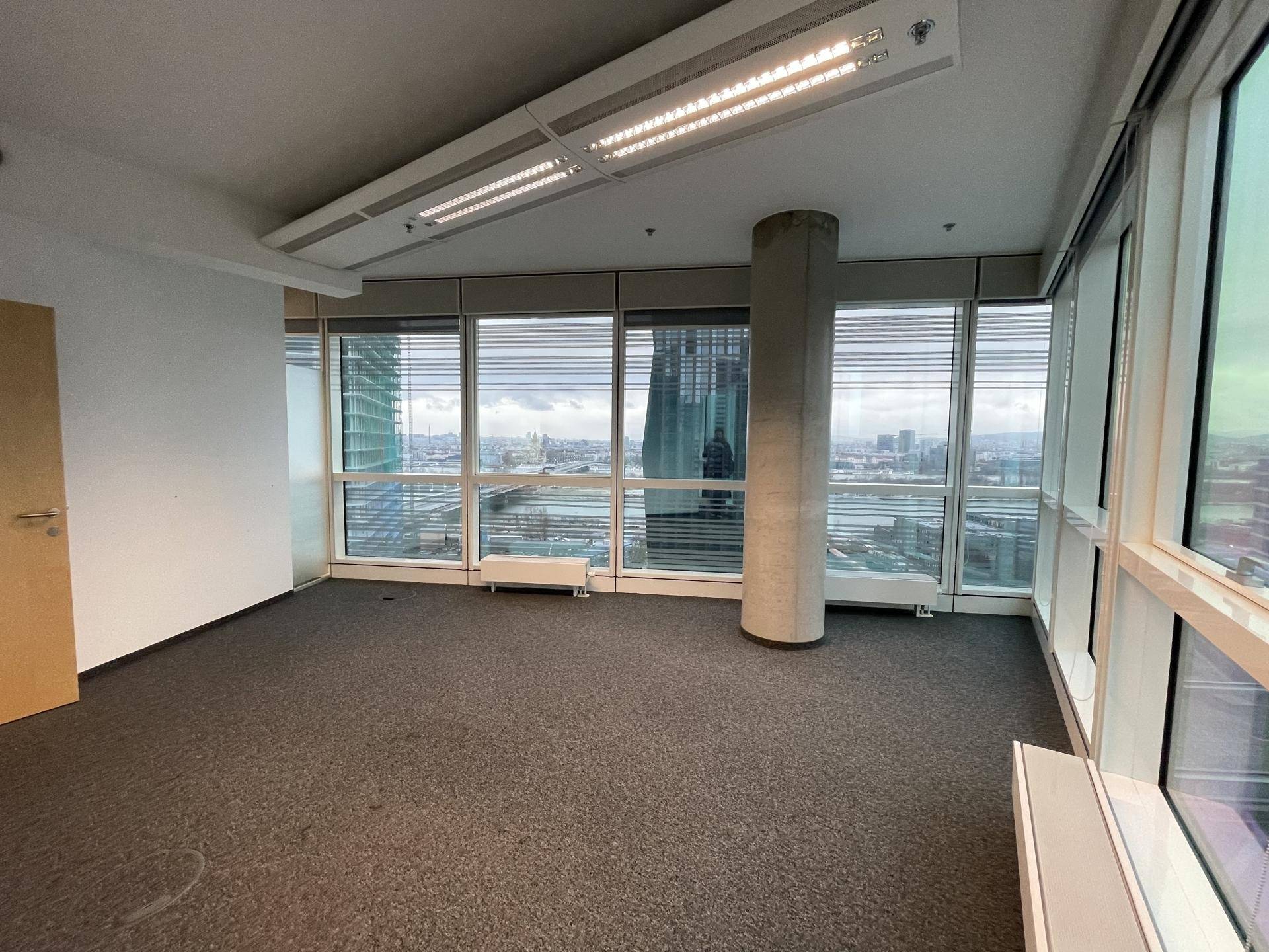 Bürofläche mit Teppichboden und Panoramablick auf die Stadt durch große Fenster.