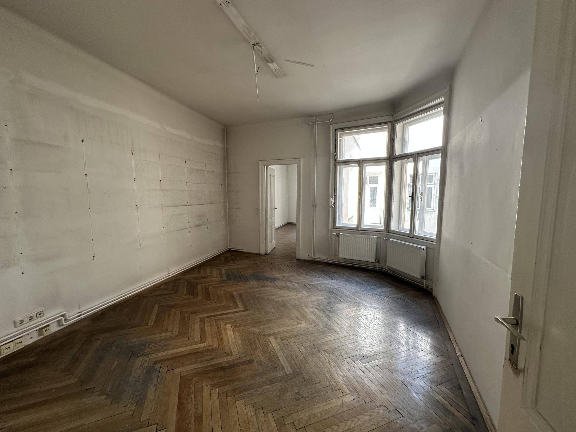 Leerer Raum mit altem Fischgrätparkett und Erkerfenster, das viel Tageslicht hereinlässt.