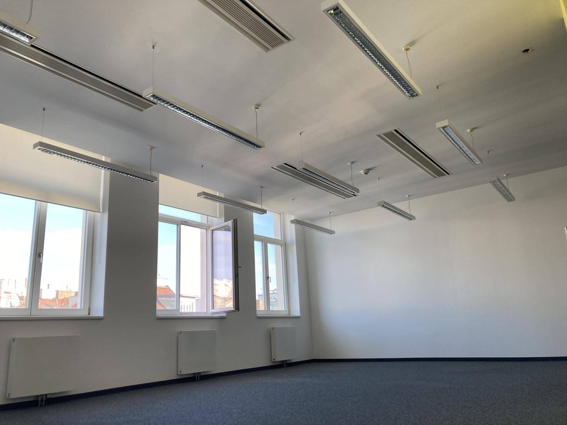 Heller Büroraum mit großen Fenstern, Teppichboden und modernen Deckenleuchten.