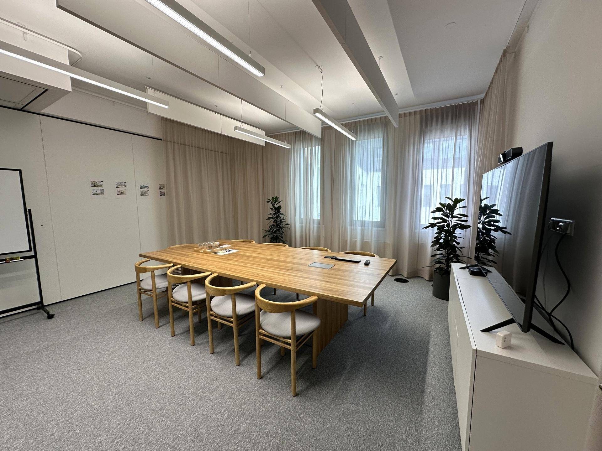 Großer Konferenzraum mit langem Holztisch, bequemen Stühlen und einem großen Bildschirm für Präsentationen.